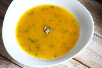 White bowl of pumpkin puree soup with greenery and seeds