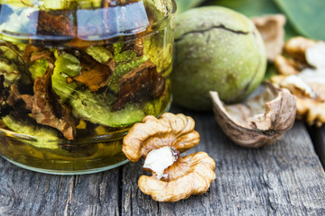 Tincture or elixir with walnuts in a glass jar on an old wooden table.