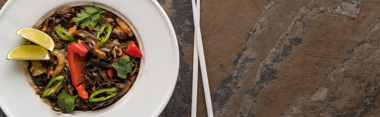 top view of thai noodles with beef near chopsticks on stone surface, panoramic shot