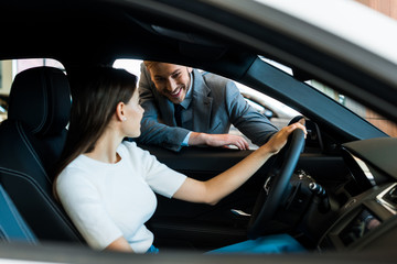 selective focus of smiling woman sitting in car near bearded man in car showroom