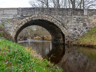 Fototapeta premium beautiful stone arched bridge over the small river, autumn day