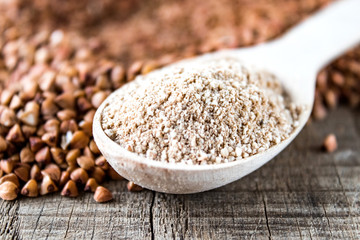 Buckwheat flour in a wooden spoon on a pile of roasted buckwheat. A pile of buckwheat flour.