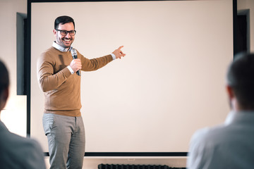 Portrait of a speaker on a seminar, talking on microphone and pointing at blank screen.