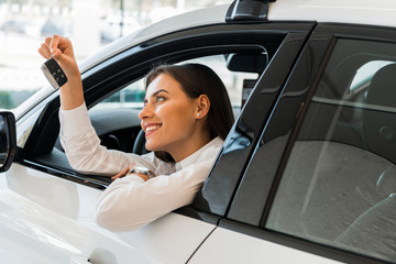 cheerful young woman holding car key while sitting in car