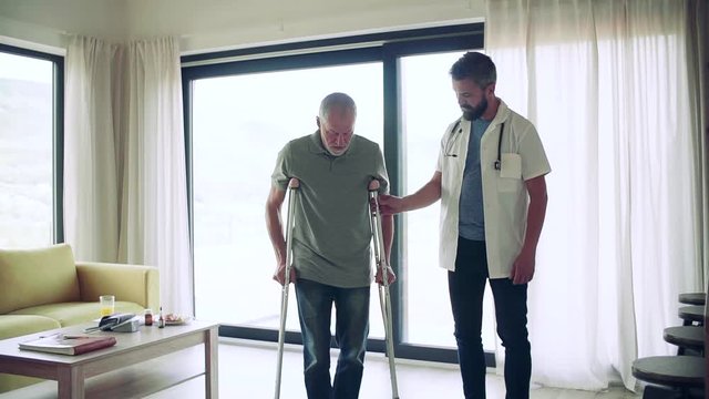 Health visitor and a senior man with crutches during home visit, walking.