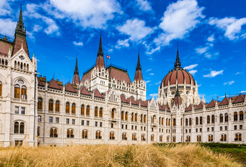 Fototapeta premium Daytime close up view of historical building of Hungarian Parliament in Budapest, Hungary, Europe with hungarian national flag on background of bright blue cloudy sky