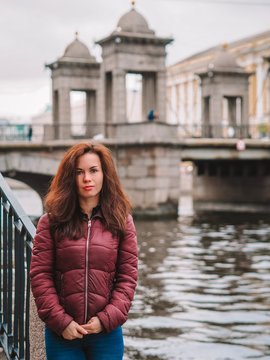 Brunette girl with long hair with backpack stands on the background of the bridge, autumn weather