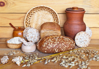 Rustic still life with traditional oat products: cereal bread, oat milk in clay jug, oatmeal and bread crisps on a wooden background. Healthy organic foods