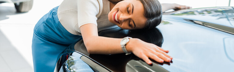 panoramic shot of happy girl with closed eyes near black car