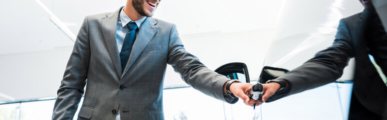 panoramic shot of happy man in suit opening car door in car showroom