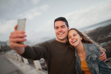 Portrait of a happy friends taking selfie on mobile phone at outdoors near the sea