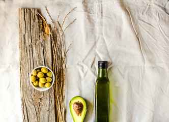 Extra virgin avocado oil in a green glass bottle. Field products. On a white linen tablecloth background. Copy space. Top view