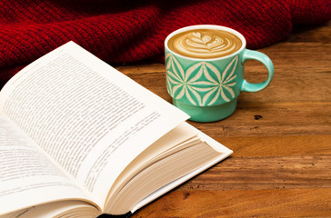 Still life details, cup of latte or cappuccino coffee with a book and red sweater on a wooden table.