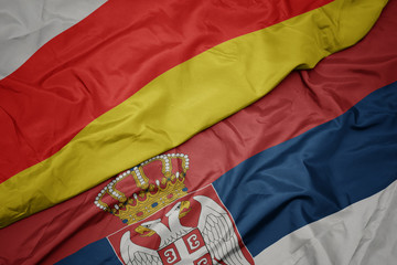 waving colorful flag of serbia and national flag of south ossetia.