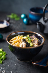 Asian ramen noodles soup with beef, oyster mushrooms and vegetables in bowl on dark background