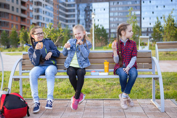 Teen girls eat on a bench in a city park.