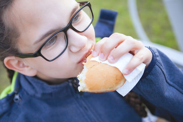 Teen girls eat on a bench in a city park.