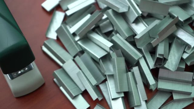 Many clips for a stapler on a wooden table. Stapler with a bunch of paper clips on the table.
