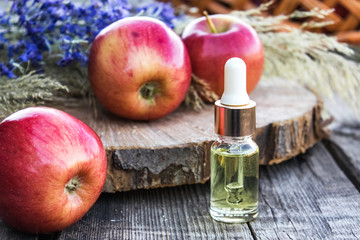 Glass bottle of apple essential oil near fresh apples on a wooden table. Essential oil is used to fill lamps, perfumes and in cosmetics.