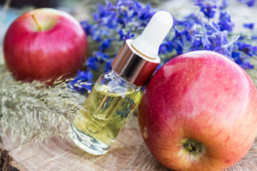 Bottle of apple essential oil and fresh apples on a wooden table. Essential oil is used to fill...