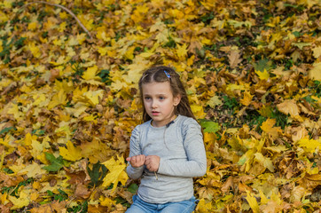 Little charming girl child throws up fallen yellow maple leaves in autumn park