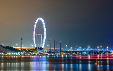 Fototapeta na wymiar The Singapore Flyer and Helix Bridge at night, colorful lightrails created by boats.
