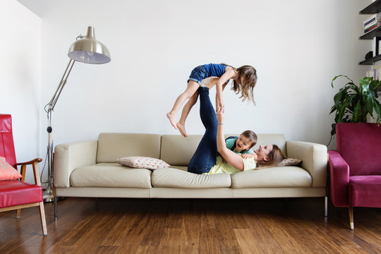 Mother holding up her daughter with her feet on sofa