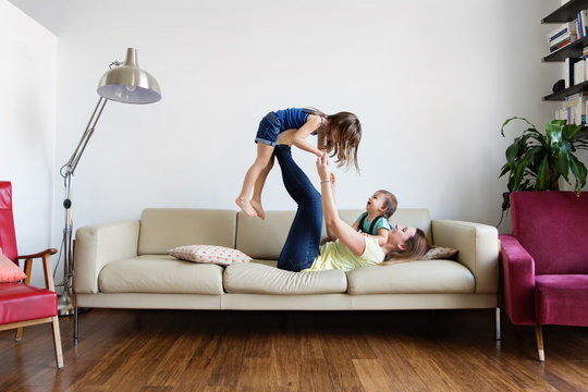 Mother playing airplane with her children on couch