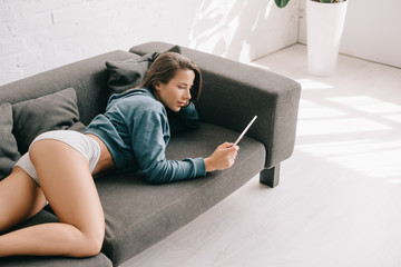 attractive sexy woman in panties using digital tablet on sofa - obrazy, fototapety, plakaty