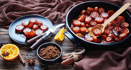 candied yams, sweet potatoes cooked with cinnamon, orange juice, brown sugar and butter in a black ceramic dish. a portion served on a black plate on a rustic wooden table,  horizontal view from above
