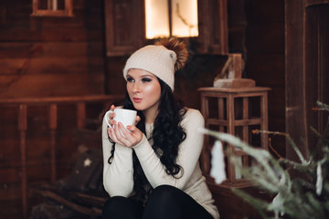 Portrait of stunning long-haired woman with smokey eyes in warm hat drinking hot tea or cacao on...