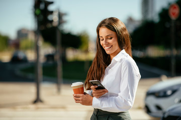 Young businesswoman drinking coffee and using phone on street 