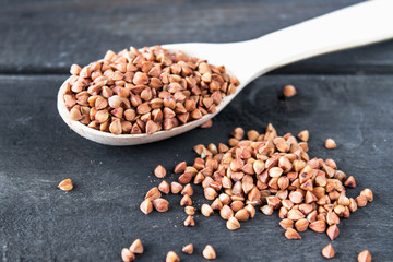 Uncooked buckwheat in a spoon on dark old boards. Buckwheat is used for cooking.