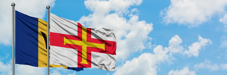 Barbados and Guernsey flag waving in the wind against white cloudy blue sky together. Diplomacy concept, international relations.