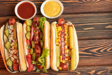 Three hot dogs with yellow mustard and ketchup on a wooden table