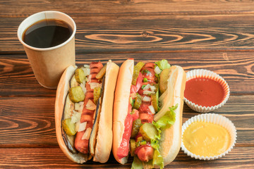 Two hot dogs with coffee, one with ketchup, one with mustard on wooden background