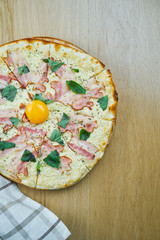 Italian, homemade carbonara pizza with mozarella cheese, yolk and bacon on a wooden table. Top view food with copy space. Flat lay