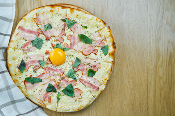 Italian, homemade carbonara pizza with mozarella cheese, yolk and bacon on a wooden table. Top view food with copy space. Flat lay