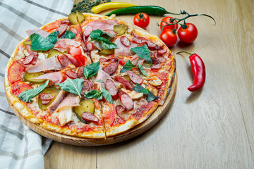 Italian, homemade sliced pizza with meat, salami, cucumber, basil and hot pepper on a wooden table. Top view food with copy space. Flat lay