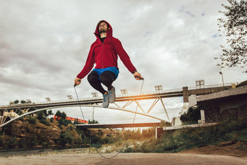 Man exercising with jump-rope outdoors , young fit guy training near the river.