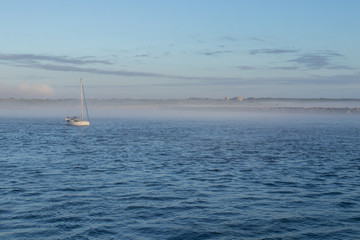 Big Catamaran Sail Boat Moored In A Calm Blue Harbour At Sunrise With Low Clouds In The Sky