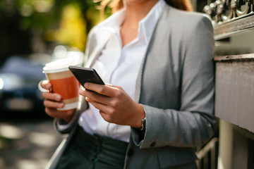 Young woman leaning on wall. Businesswoman drinking coffee and using phone.