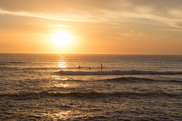Fototapeta na wymiar Golden Orange Sunrise With Waves Crashing And People On Kayaks And Paddle Boards In The Distance With Salt Spray In The Air