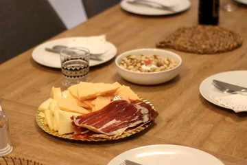 Table set for dinner party with plates, bread, prosciutto and cheese. Selective focus.