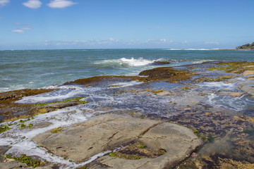 Rocky Shoreline Rock Pools Covered In Red Green Algae Seaweed And Marine Organisms By Blue Crashing Ocean Waves On A Sunny Day