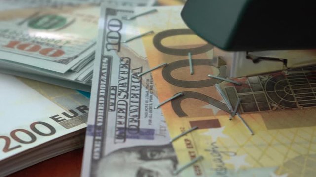 The stapler fastens the dollar and euro notes with iron clips. Stapler with paper clips on the background of banknotes. Counterfeit money
