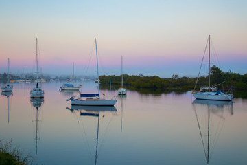 Obraz premium Sail Boats Moored On A Calm Water River At Sunrise With Pink Blue And Orange Pastel Skies
