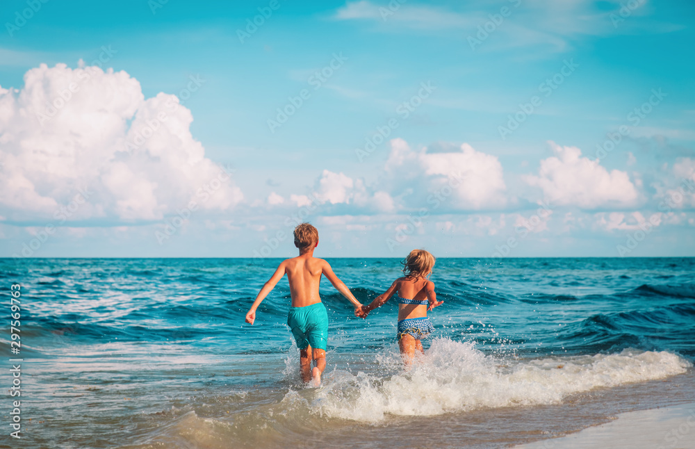 Wall mural happy girl and boy run play with waves on beach