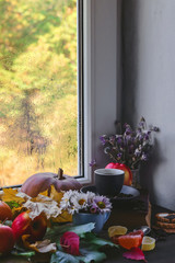 cup of coffee, autumn leaves and apples on a window background.