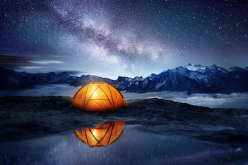 Camping adventure in the mountains. A tent pitched up and glowing under the milky way. Photo...